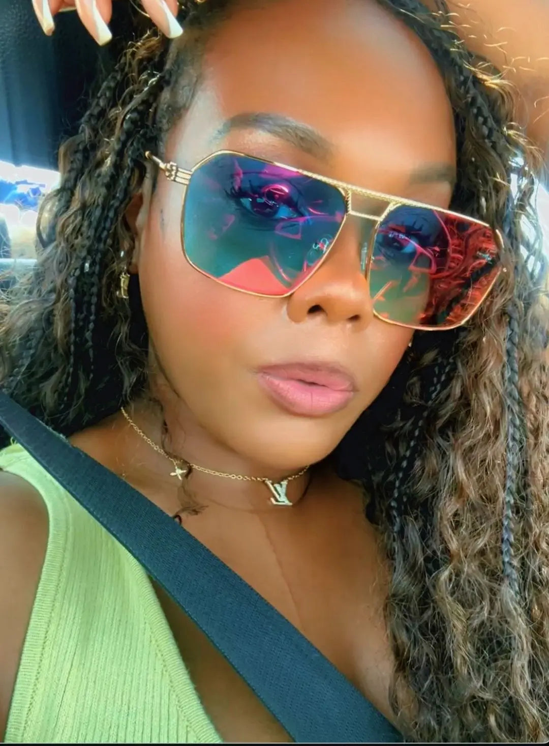 Woman wearing reflective sunglasses and a green top, sitting in a vehicle.