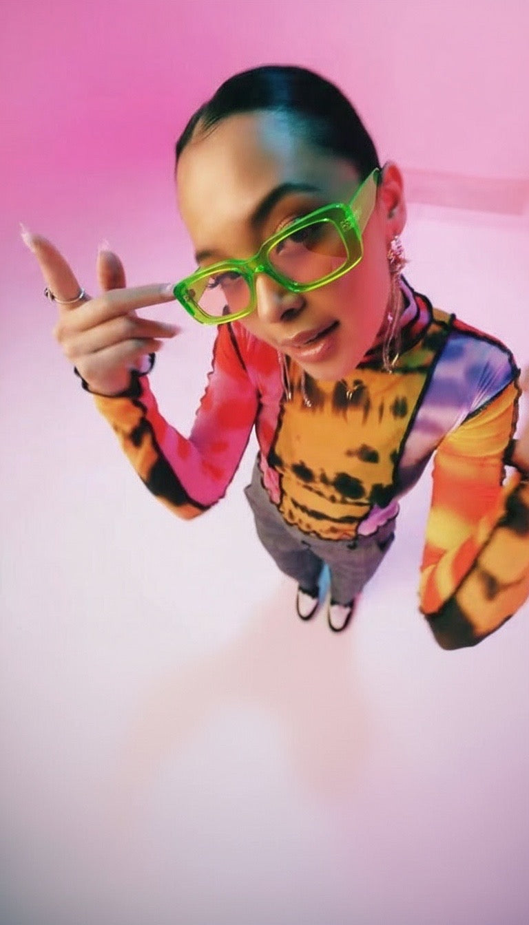 Person wearing colorful clothing and green glasses against a pink background