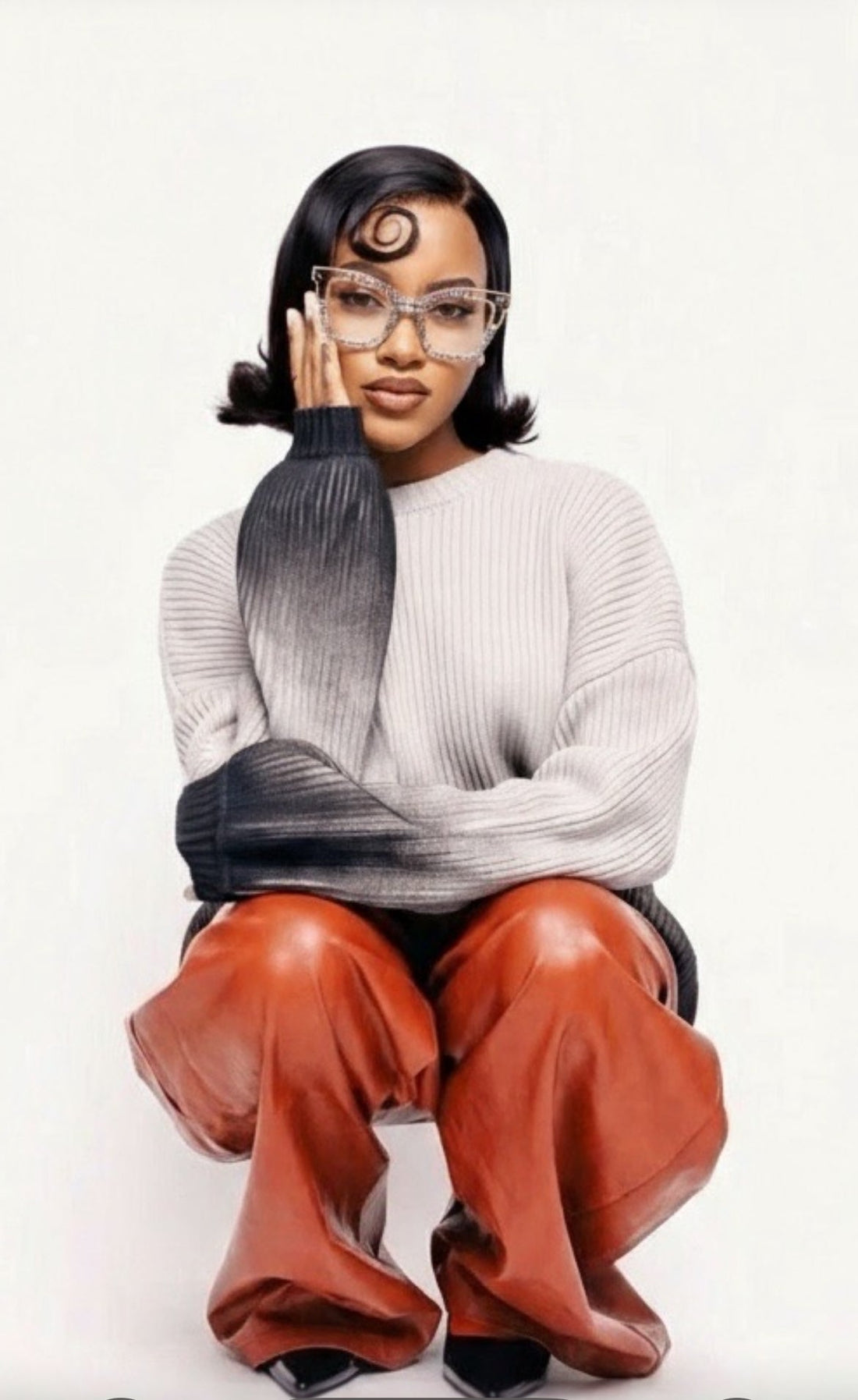 Person wearing a gray sweater with a black and gray gradient arm, orange pants, and glasses on a white background