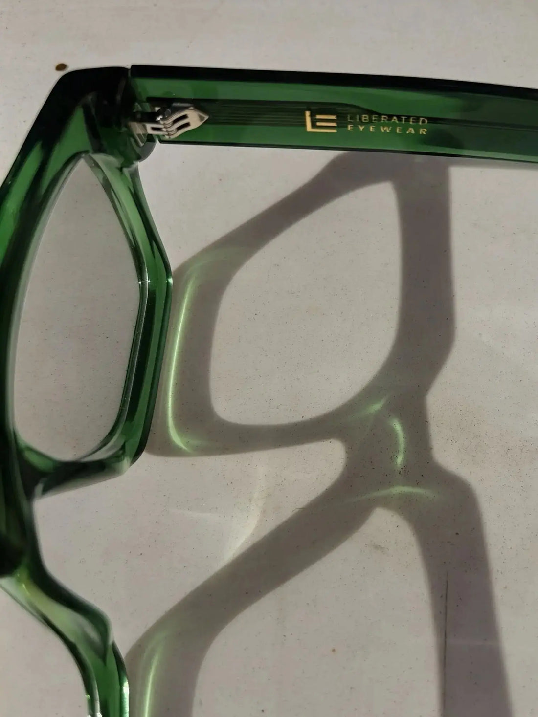 Liberated Eyewear, Inc. Jade rectangular green translucent acetate frames casting a sharp shadow on a white surface.