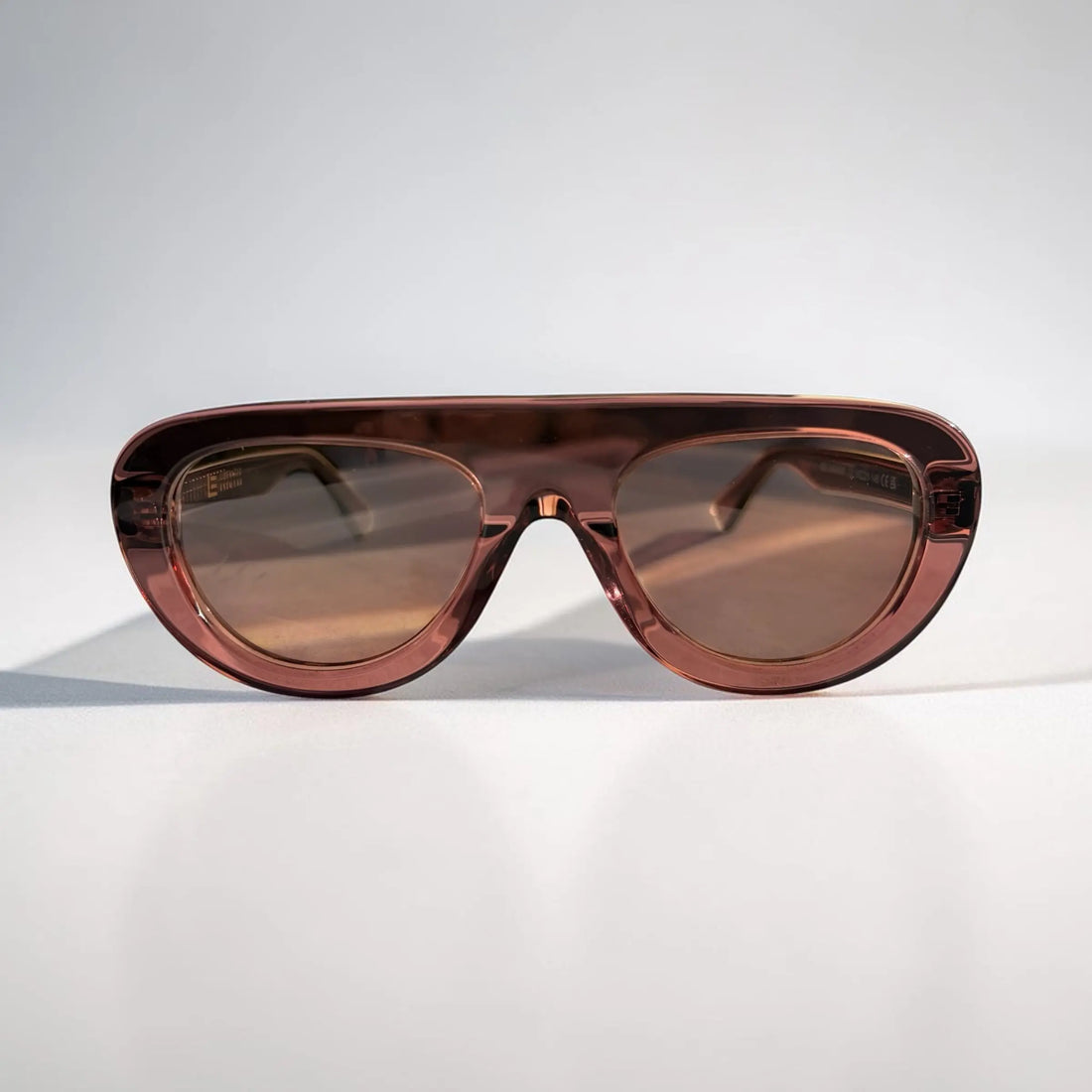 A pair of oversized shield-style sunglasses with a translucent reddish-brown acetate frame and matching tinted lenses, photographed on a clean light gray studio background.