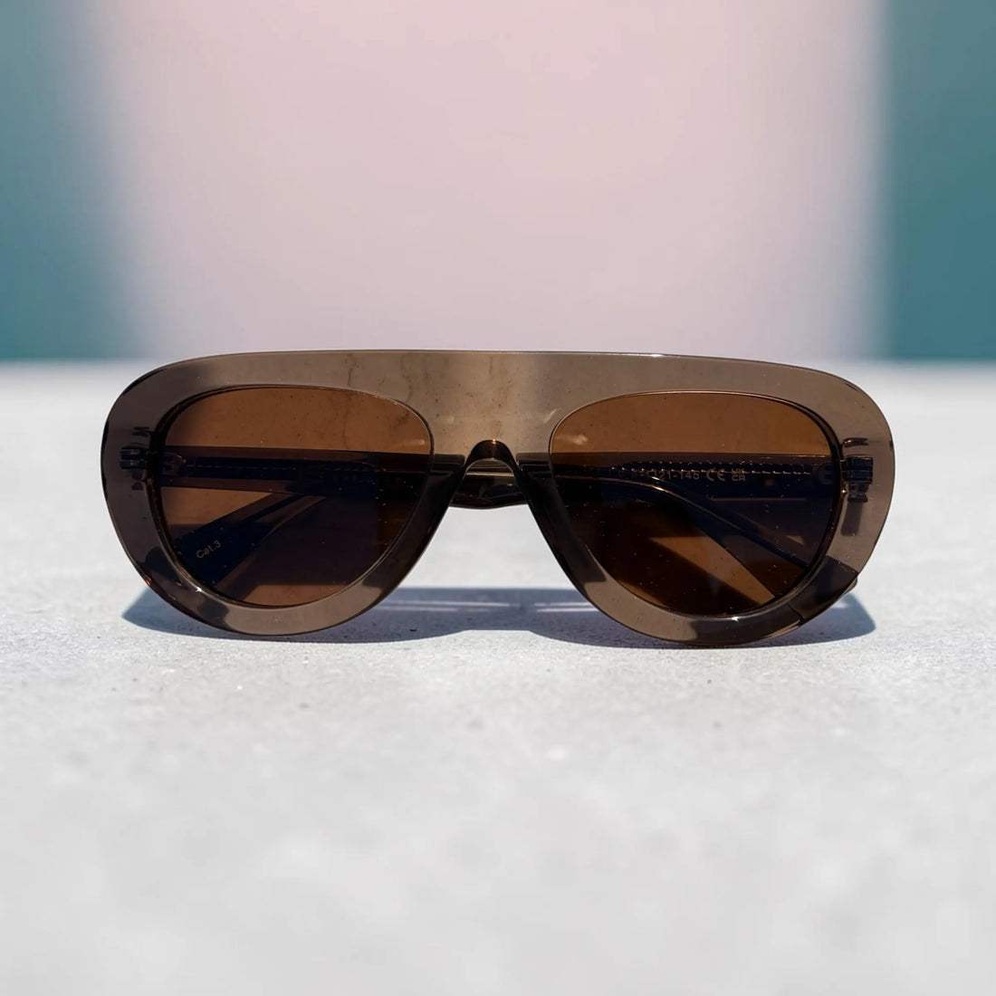 A pair of oversized aviator-style sunglasses with a translucent smoky brown frame and dark brown lenses, resting on a light textured surface.